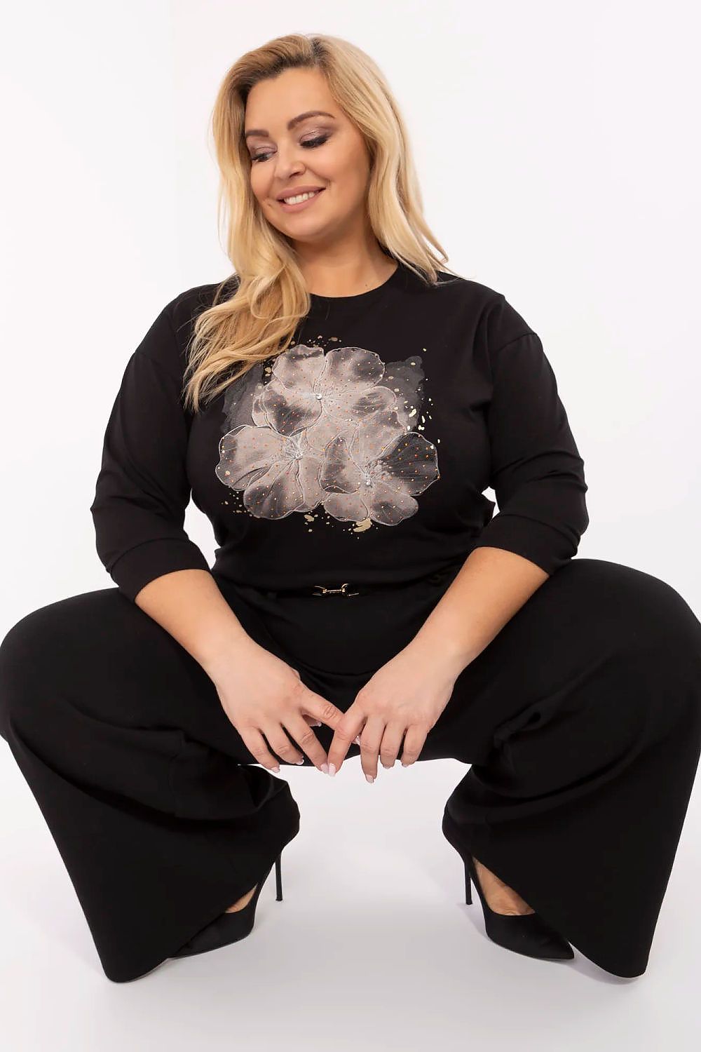 Mulher plus size vestindo blusa preta plus size com estampa floral prata e calça preta