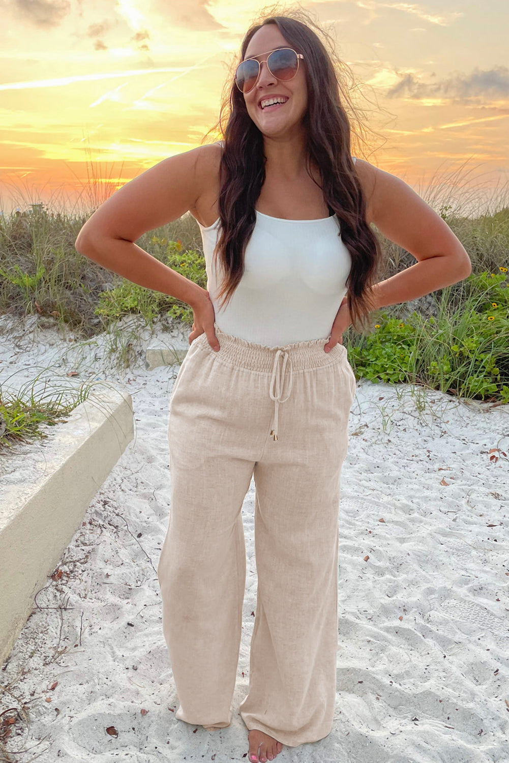 Mulher usando calça plus size com babado e elástico bege ao ar livre em ambiente de praia ao pôr do sol