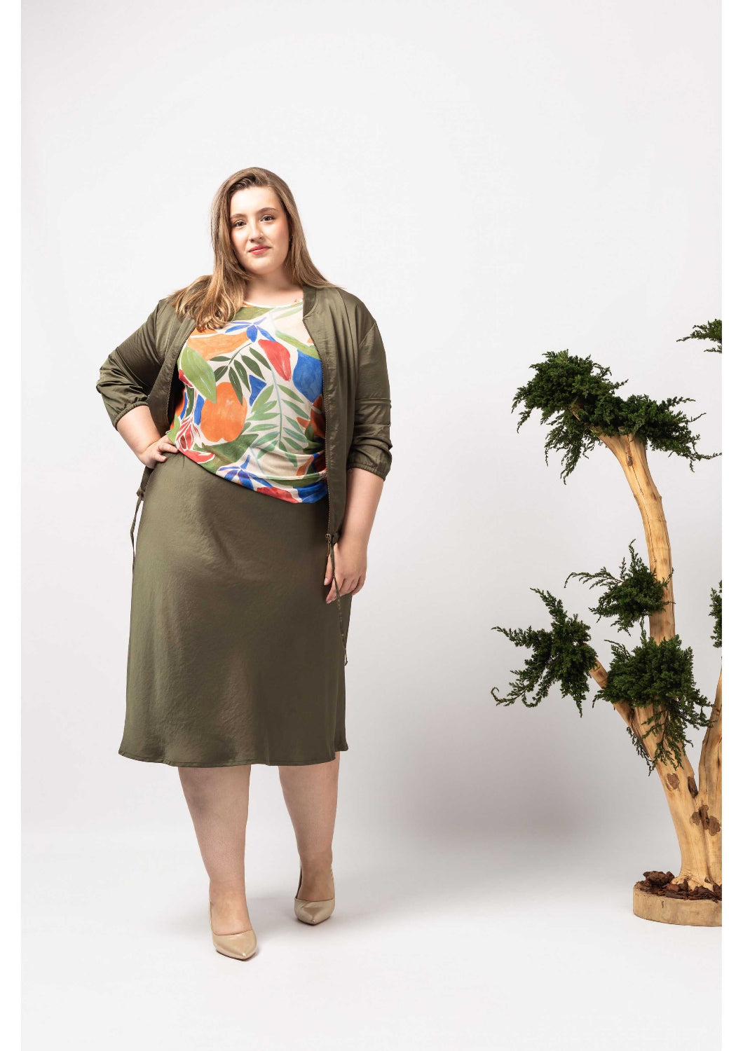 Mulher plus size usando casaco acetinado feminino verde com saia midi e blusa estampada colorida