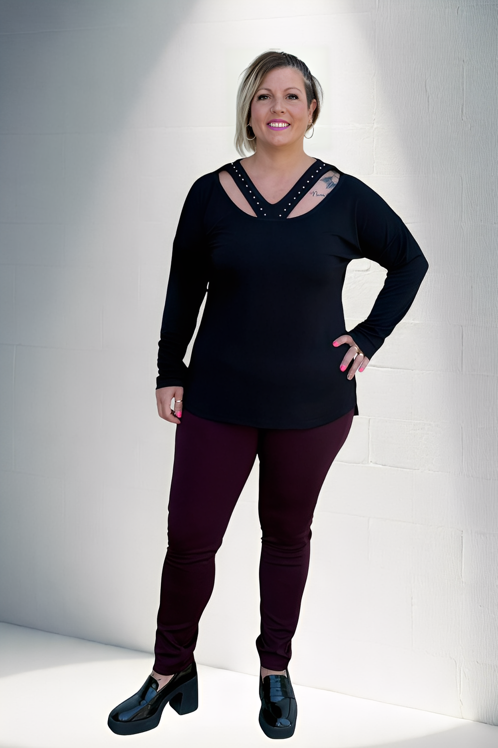 Modelo plus size usando camisola casual feminina plus size preta com decote em tiras mangas longas e calça vinho