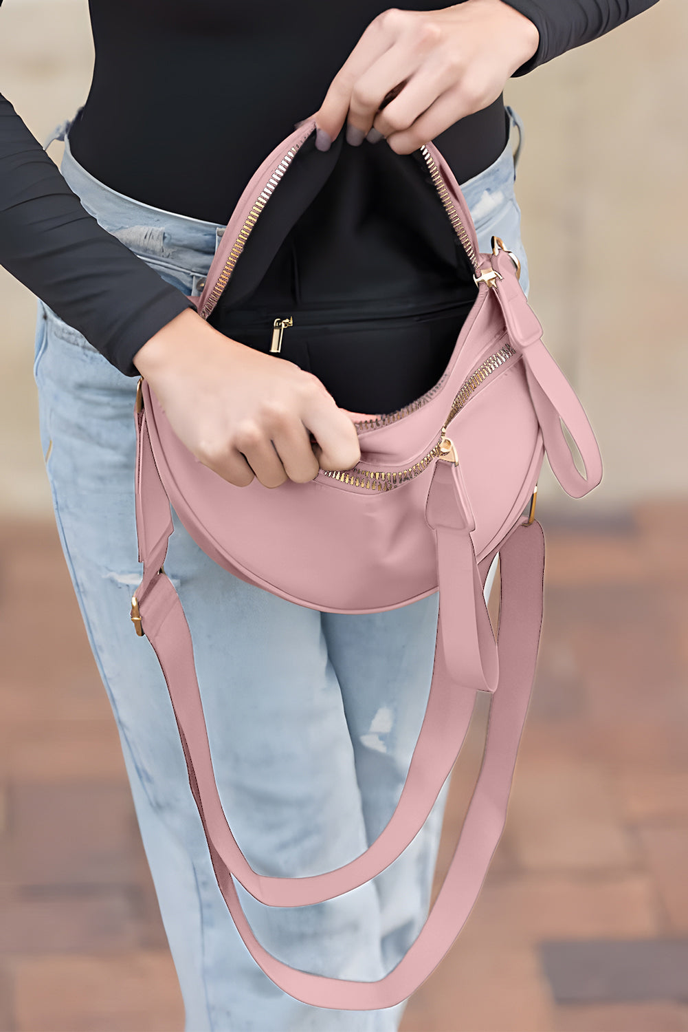 Bolsa transversal feminina com ziper rosa sendo aberta por mulher vestindo blusa preta e jeans