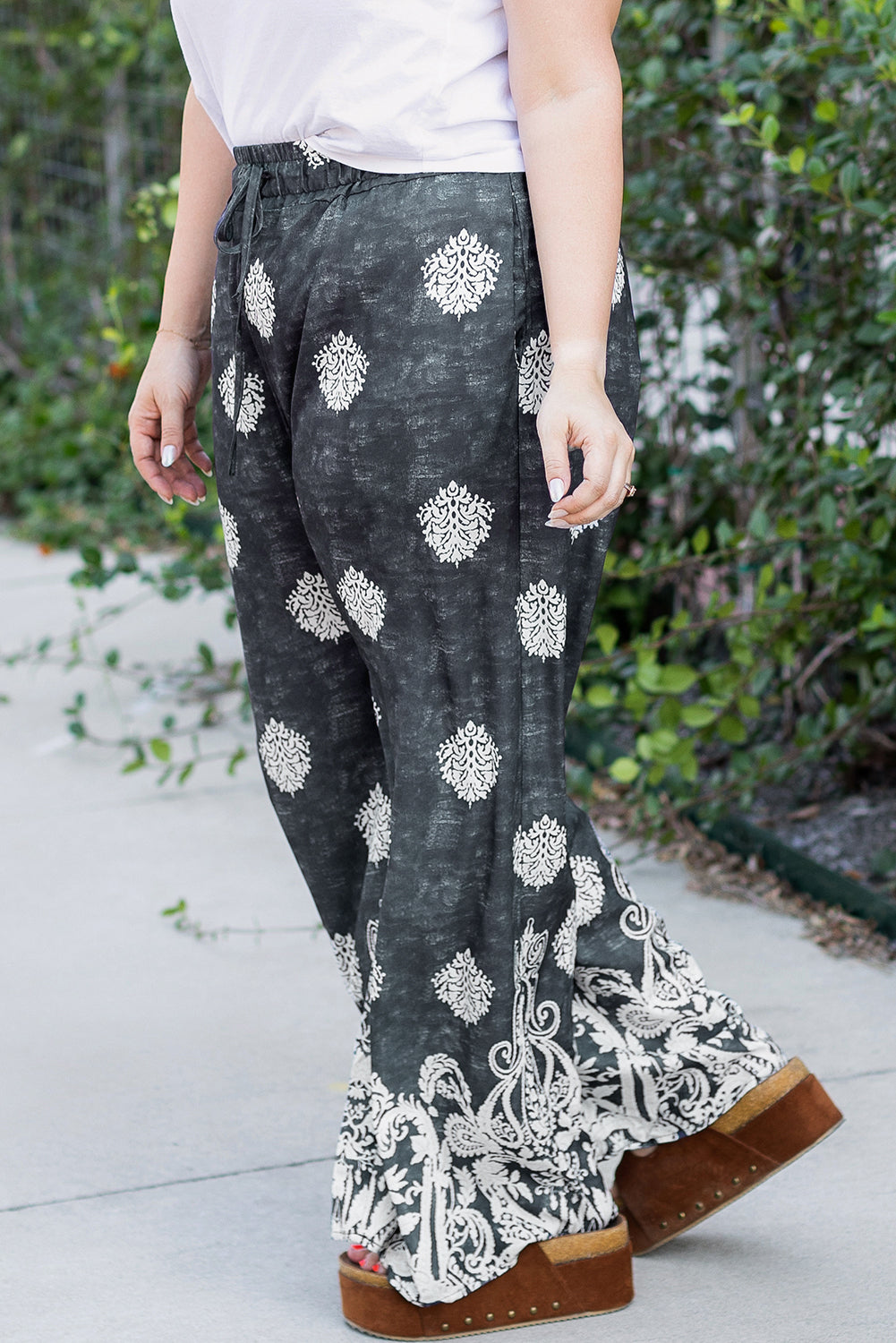 Pantalona plus size estampada preta com design floral branca usada com sandálias de plataforma