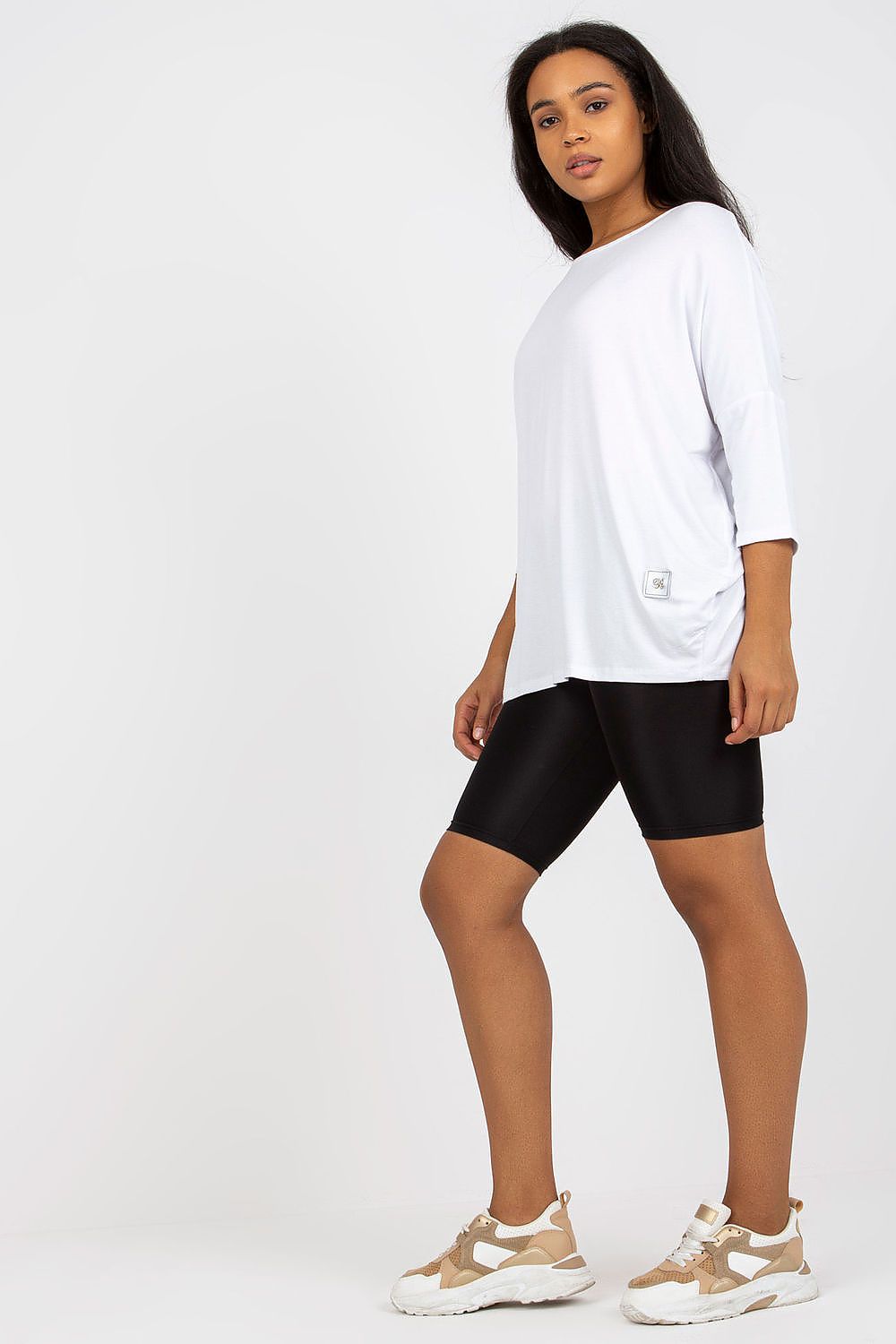 Mulher usando blusa tamanho grande moda curvy branca com bermuda preta e tênis bege