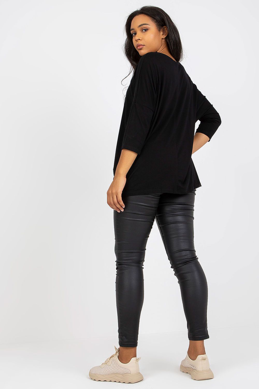 Mulher vestindo blusa tamanho grande moda curvy preta com calça preta justa e tênis bege
