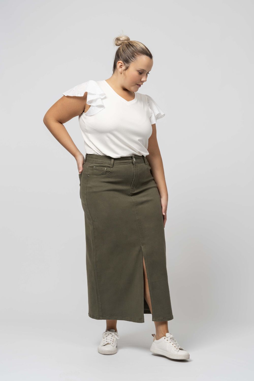 Mulher usando saia denim comprida com racha verde oliva da Curvy com camiseta branca e tênis