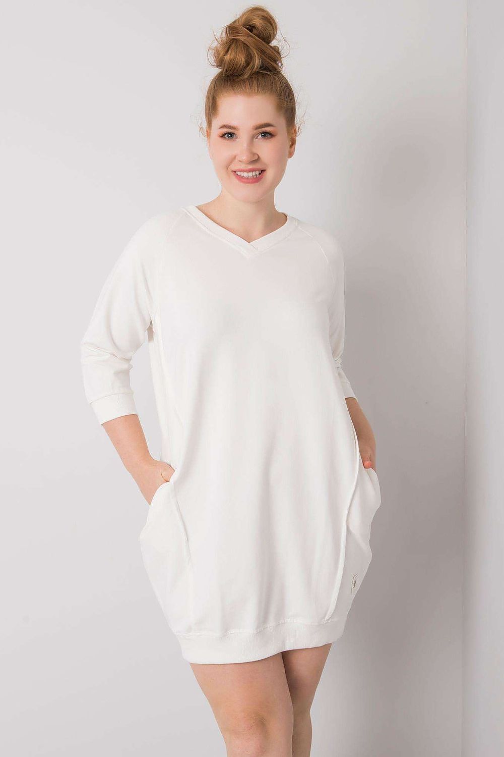 Vestido casual plus size com bolsos em branco, modelo soprando cabelo preso e sorriso suave