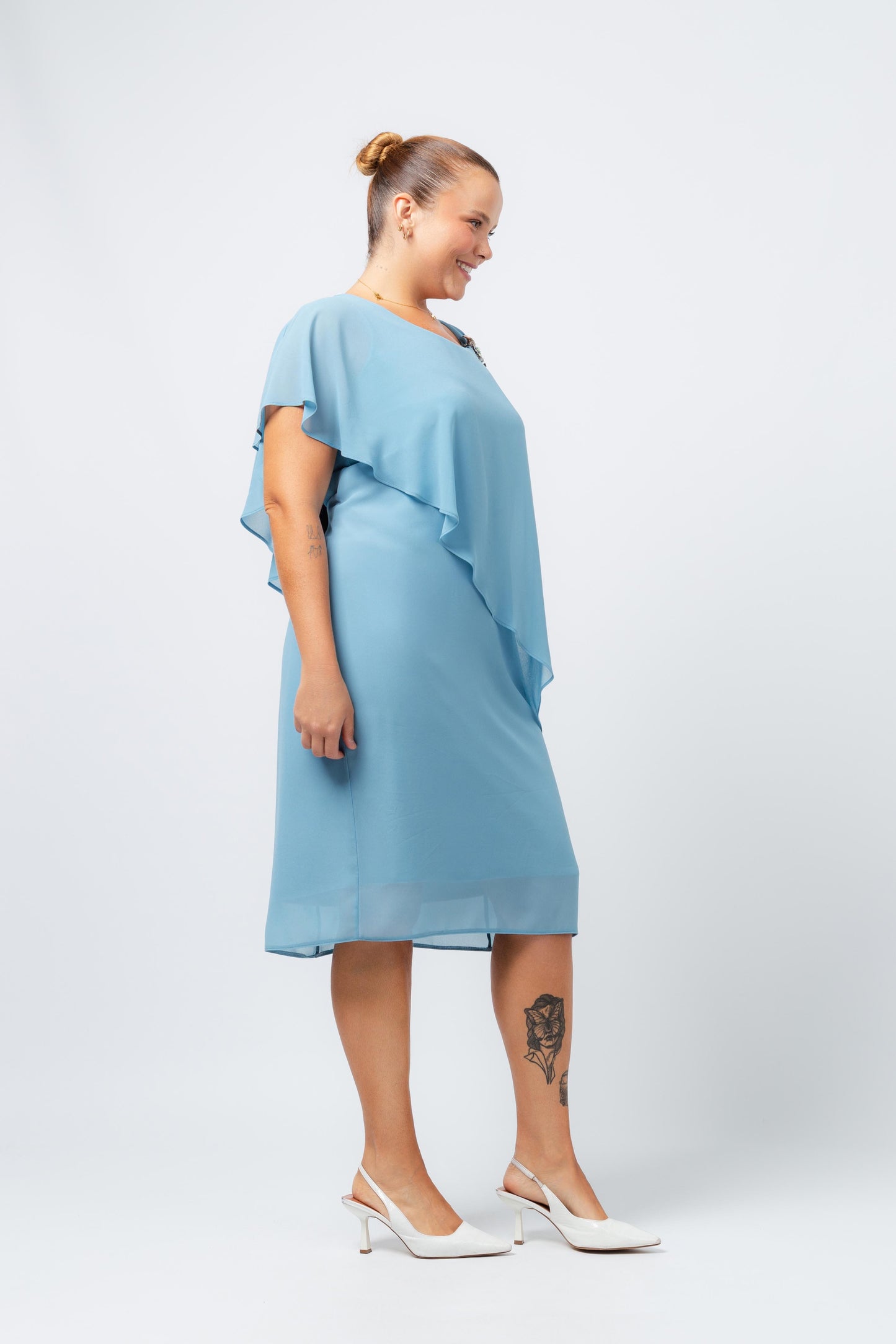 Vestido elegante com capa sobreposta azul da Curvy, modelo plus size com sapatos brancos