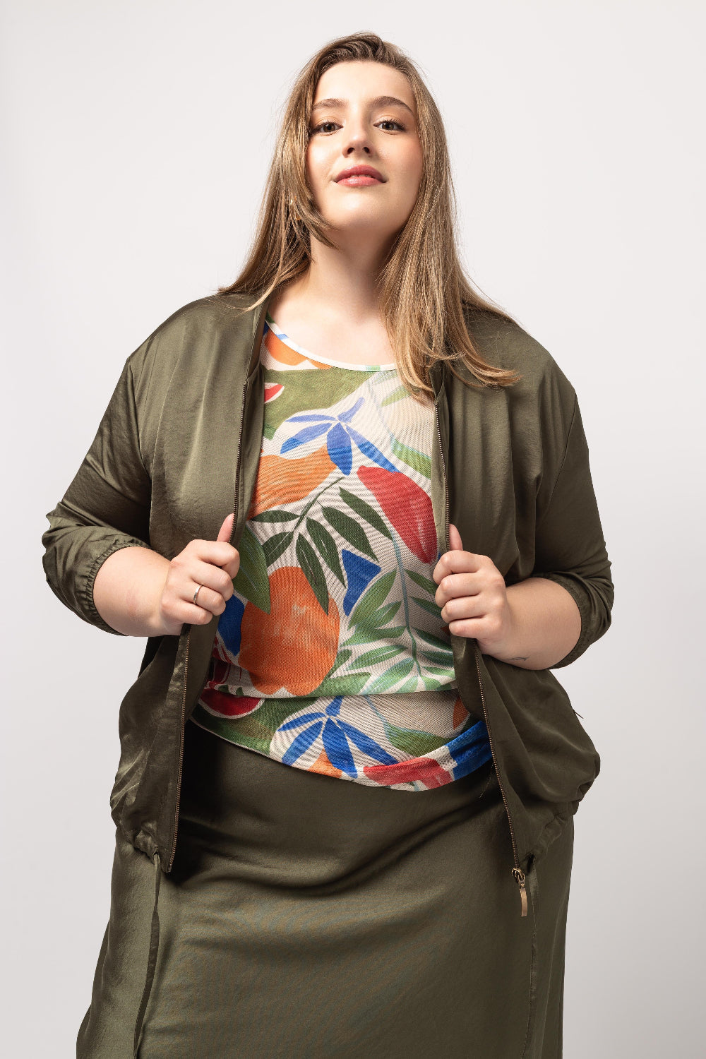 Mulher plus size usando casaco acetinado feminino verde com zíper aberto e blusa estampada colorida