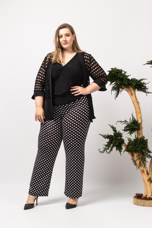 Mulher usando casaco de renda furada para mulheres preto da Curvy com calça preta de bolinhas brancas