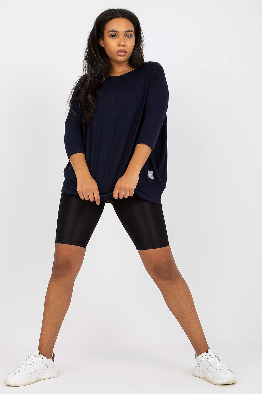 Mulher vestindo blusa tamanho grande moda curvy azul marinho com calça preta ciclista e tênis branco