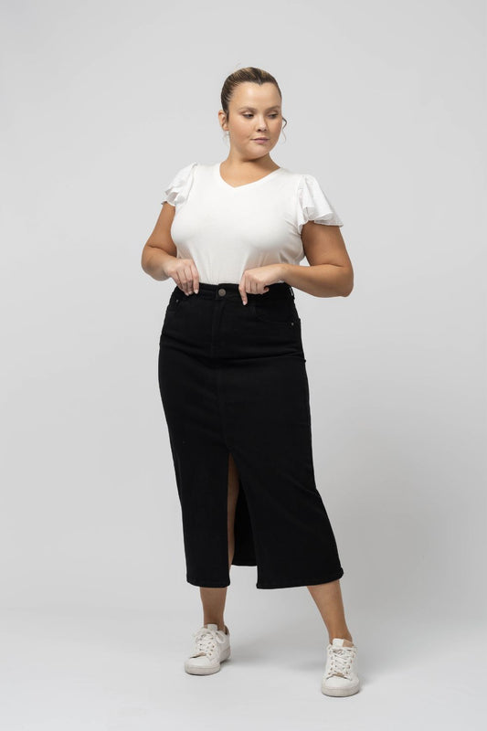 Modelo veste saia denim comprida com racha preta da Curvy combinada com camiseta branca e tênis