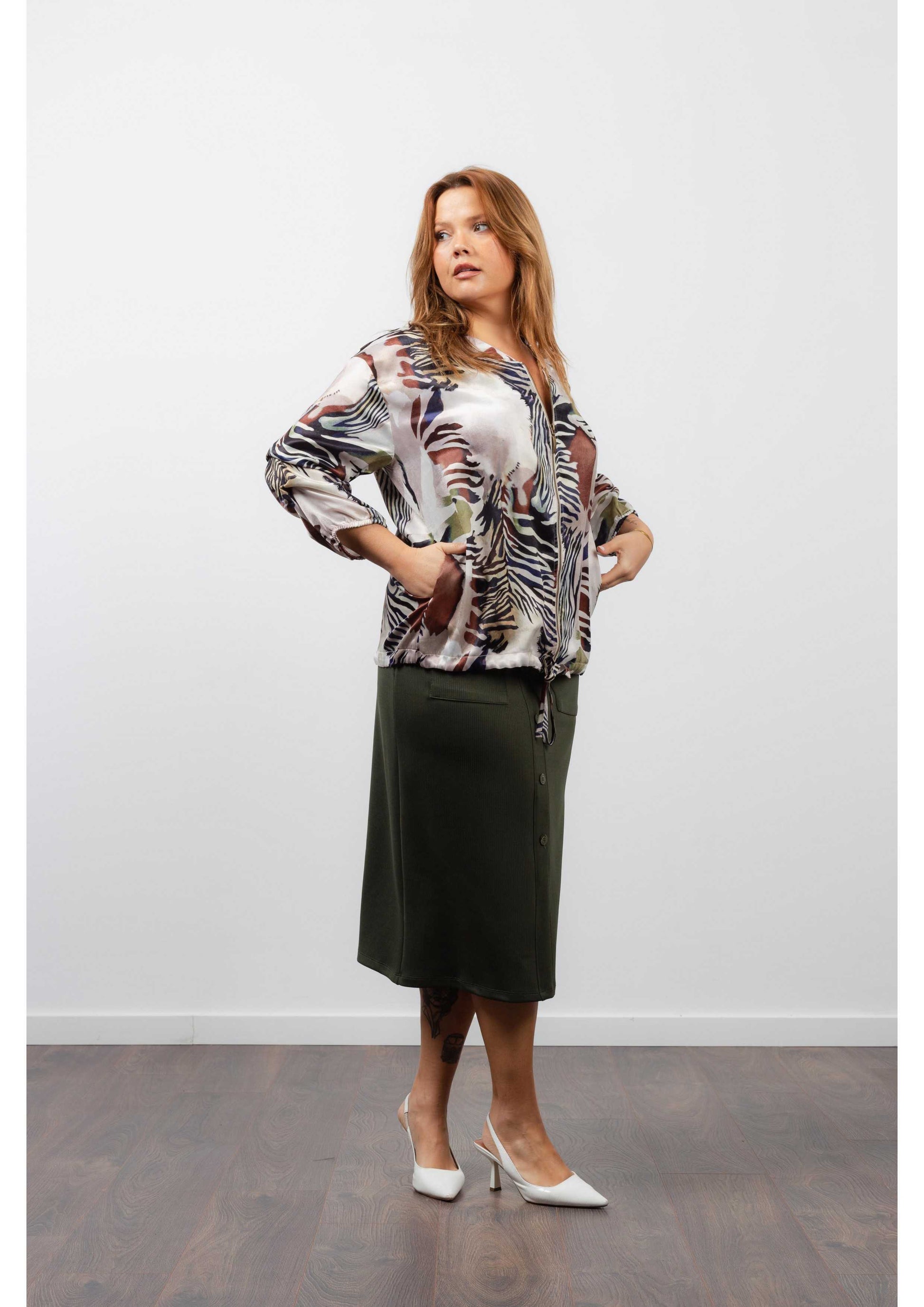 Mulher vestindo saia midi feminina canelada verde combinada com blusa estampada e salto branco