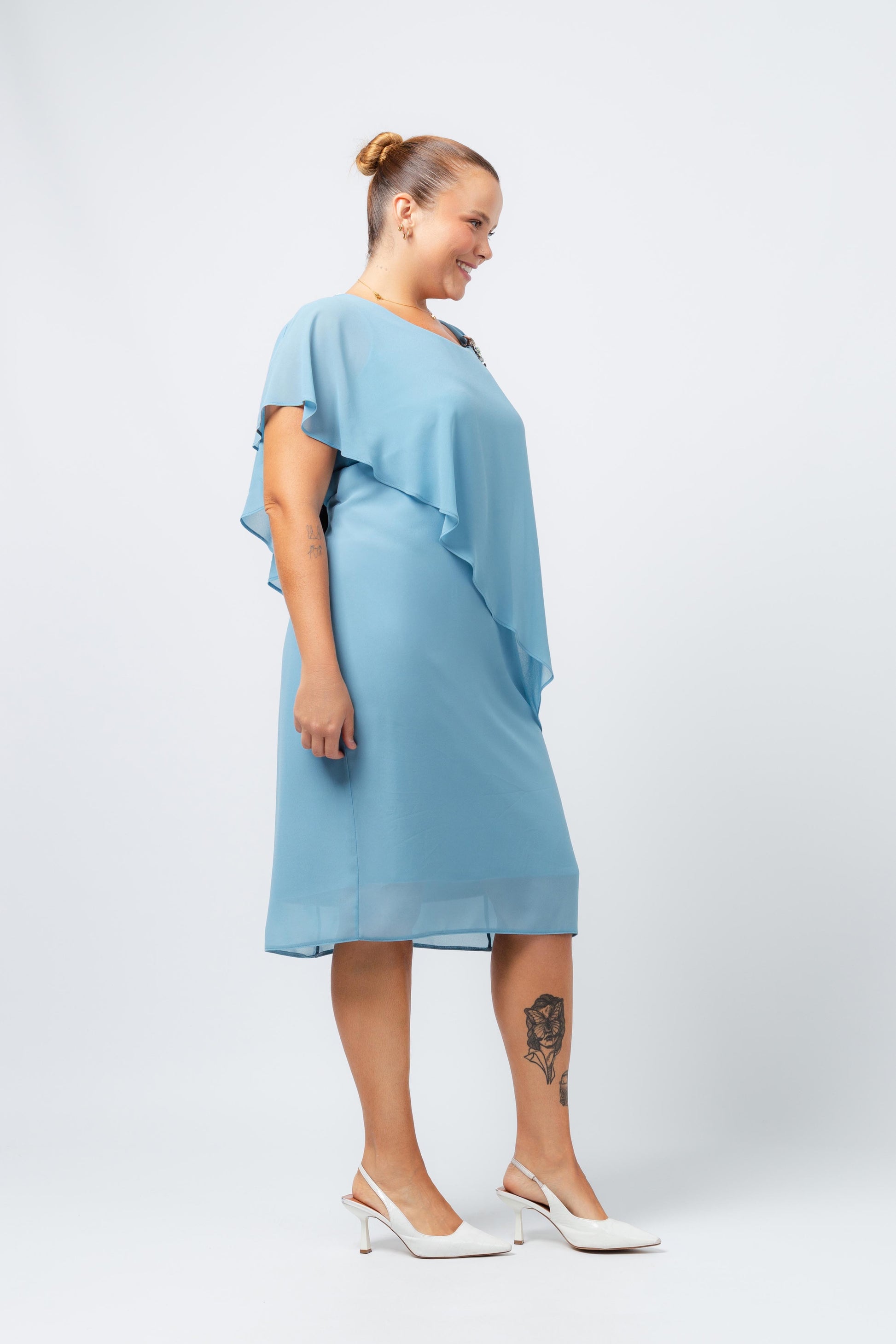 Vestido elegante com capa sobreposta azul da Curvy, modelo plus size com sapatos brancos