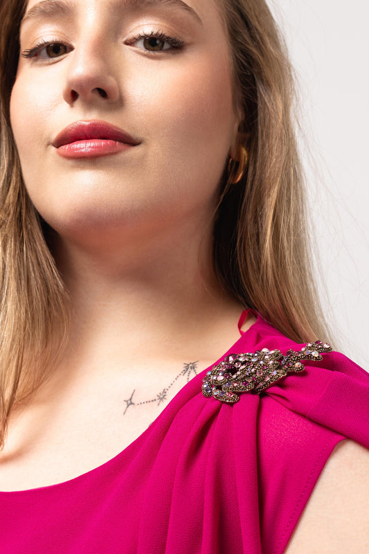 Detalhe do vestido elegante com capa sobreposta em tom rosa vibrante da Curvy com broche decorativo
